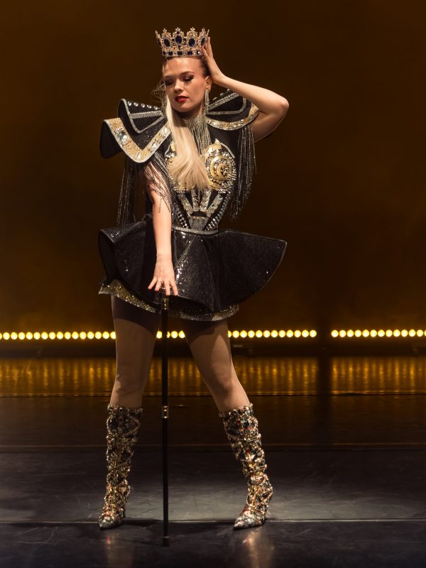 danseuse cabaret pose sur scène en tenue noir et or avec couronne et sceptre
